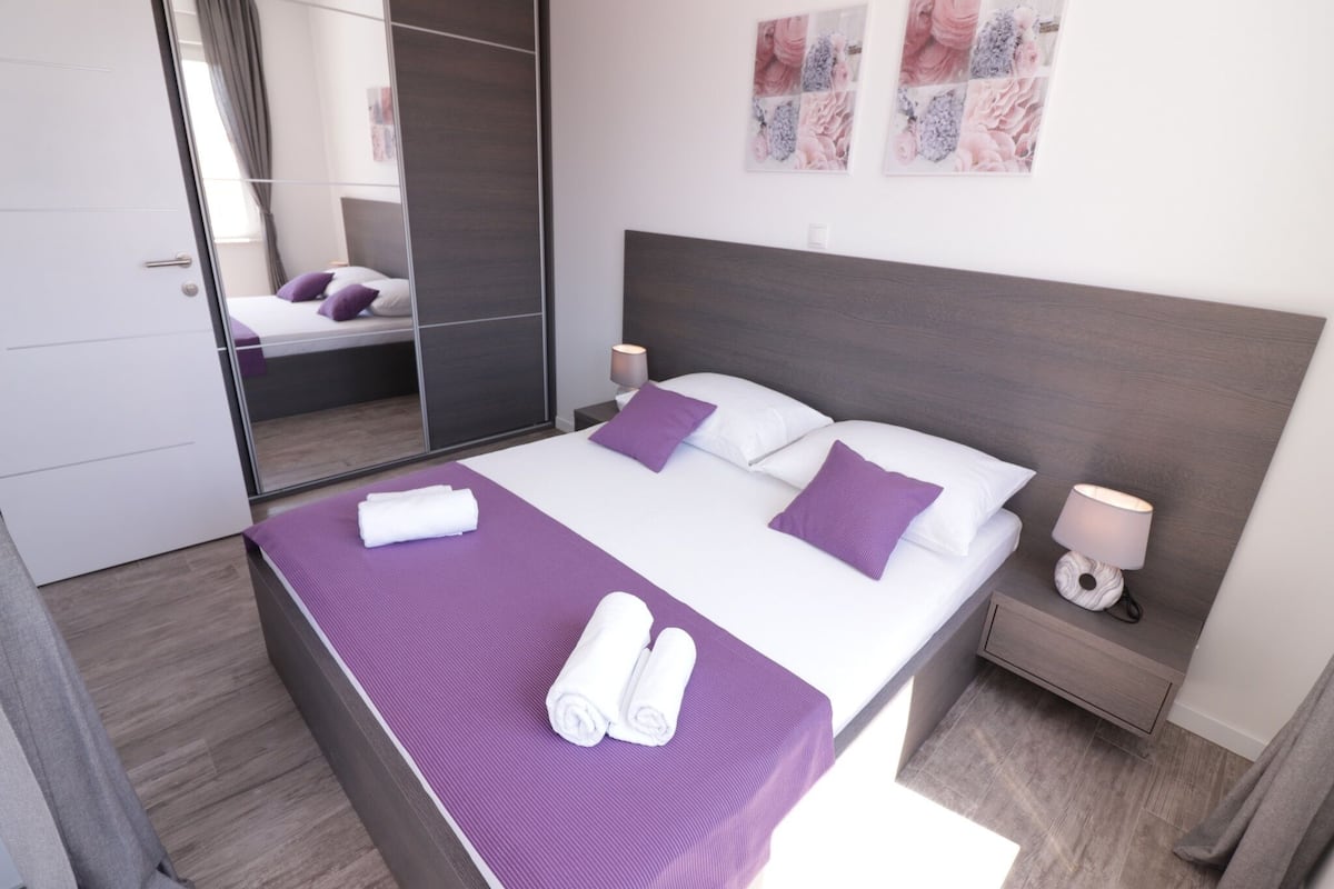 A modern bedroom with a large bed, a bedside table with a lamp, and a mirror.