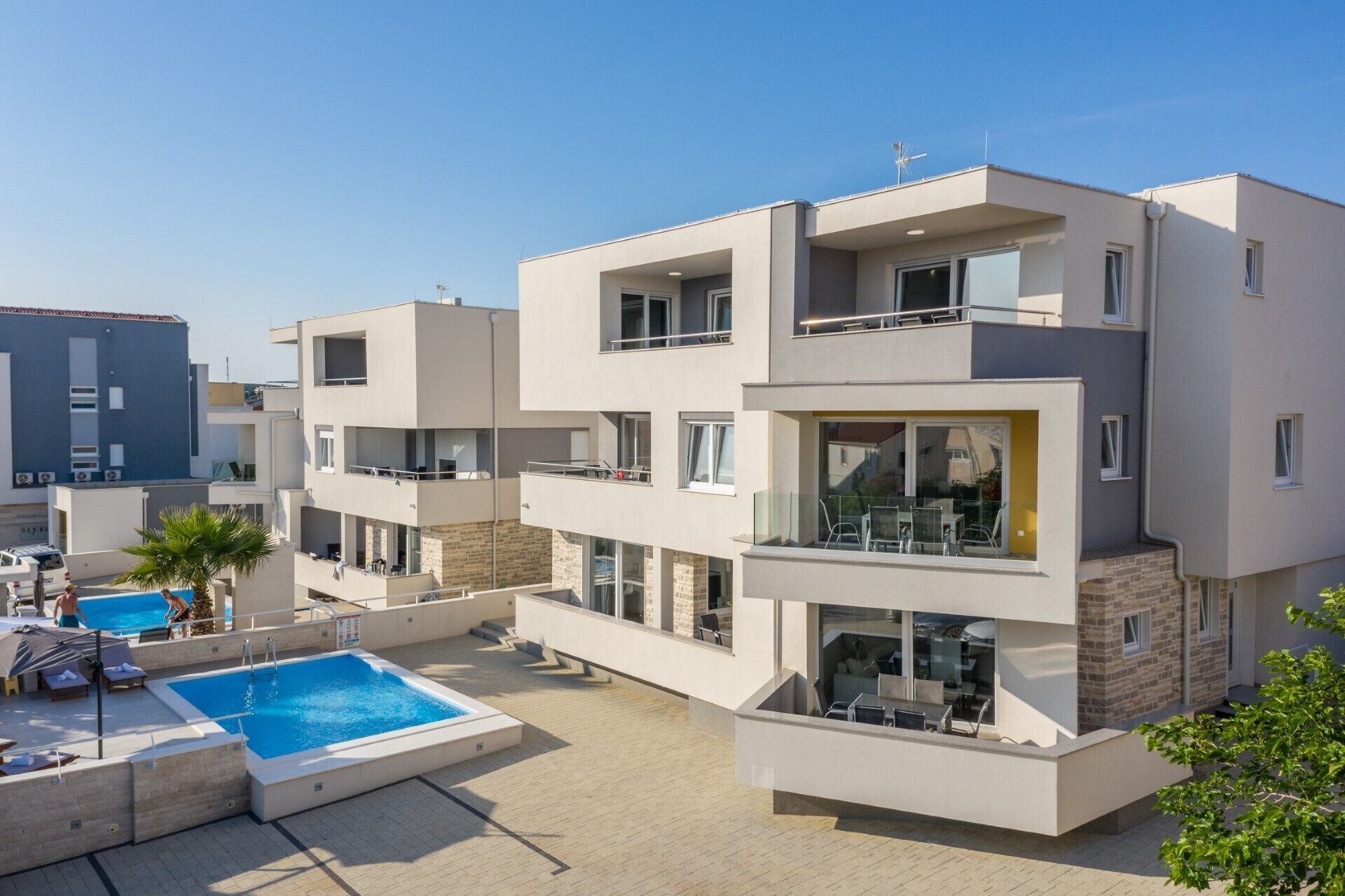 Un moderno edificio residencial de varios pisos con piscina, balcones y cielo despejado.