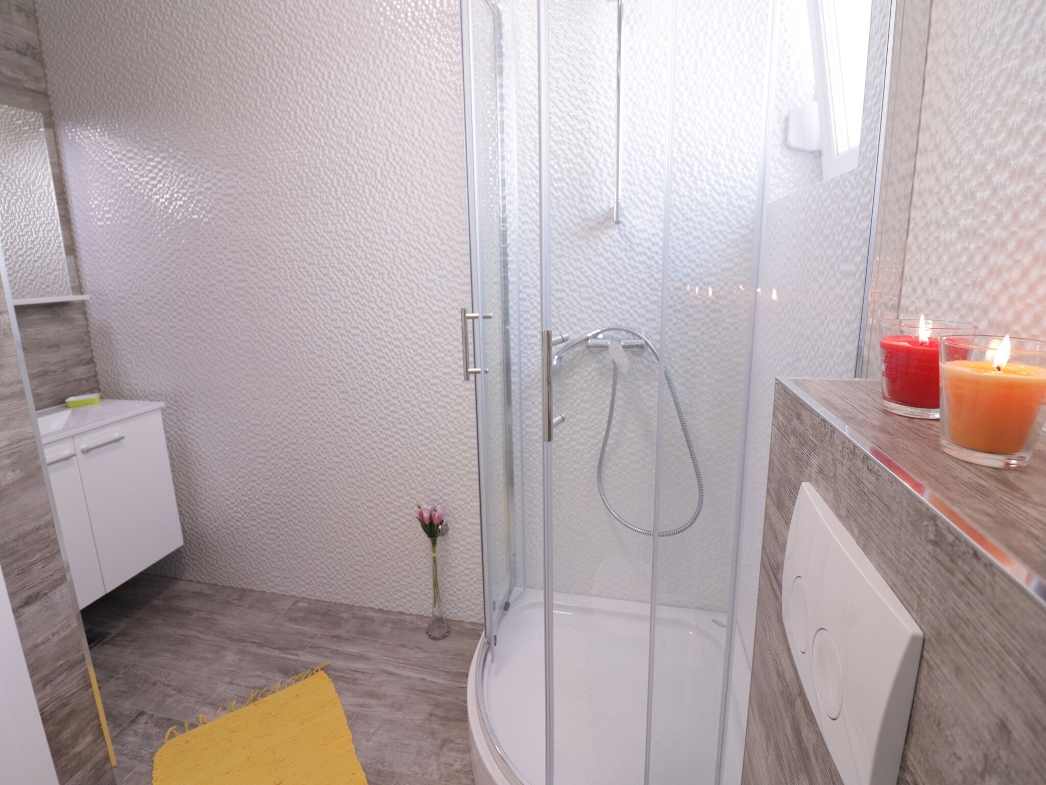 A modern bathroom with a glass shower enclosure, a white sink, and a yellow rug.