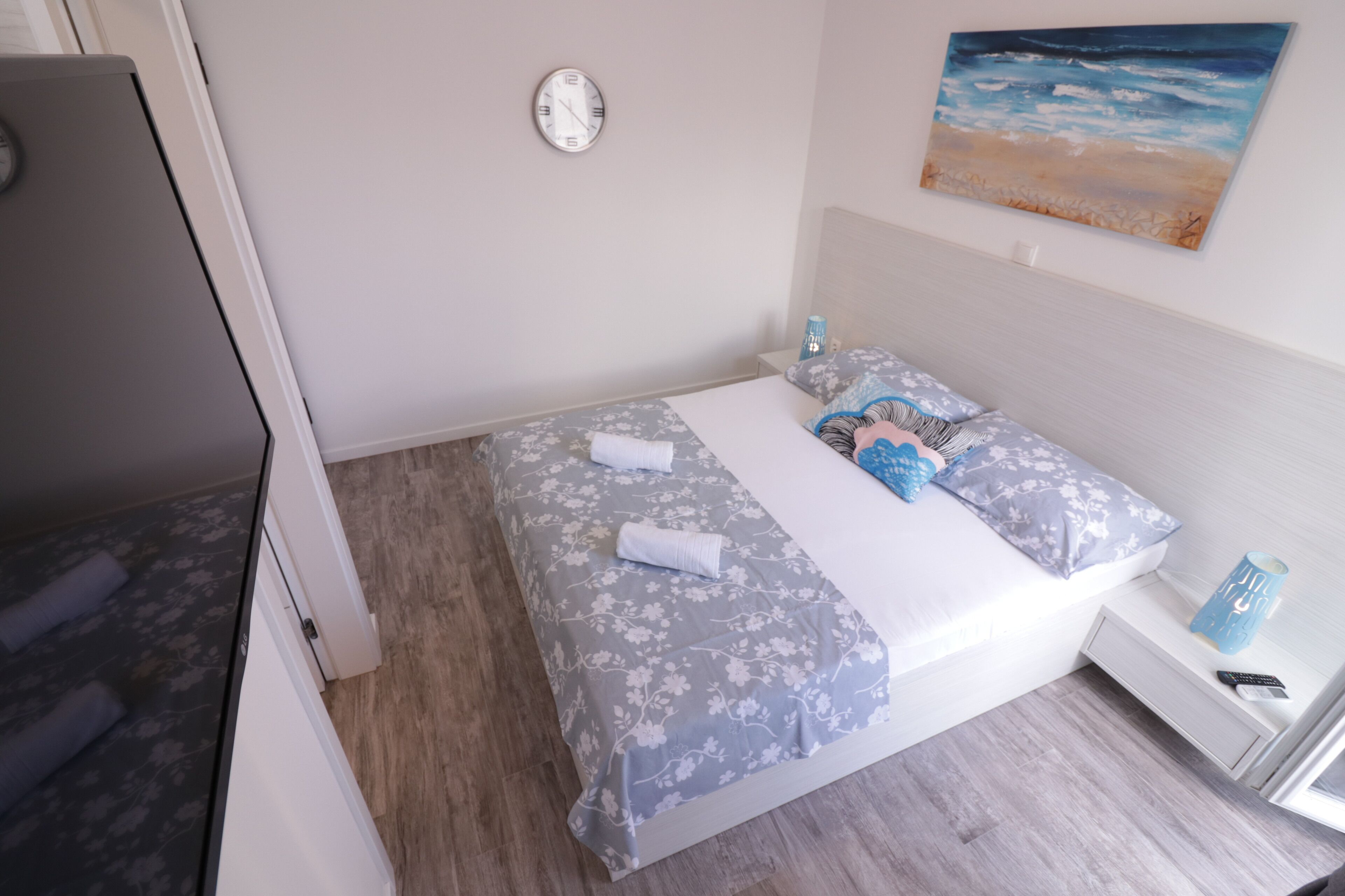 Un dormitorio con cama, mesita de noche, reloj y un cuadro en la pared.