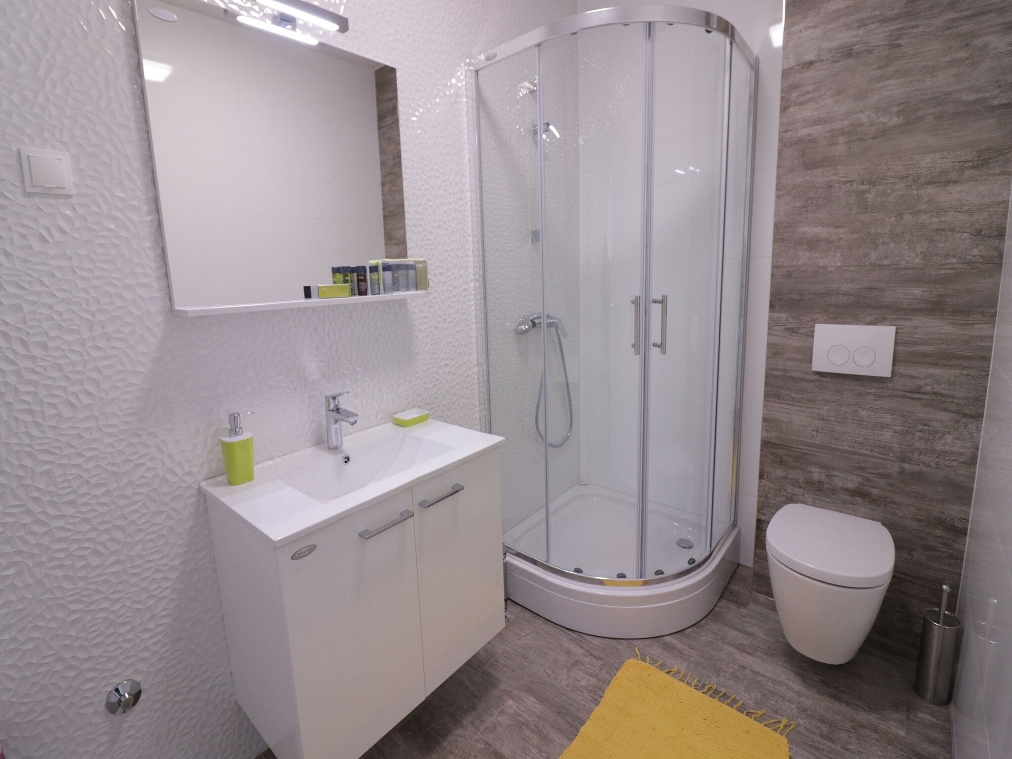 A modern bathroom with a white vanity, a glass shower enclosure, and a white toilet.