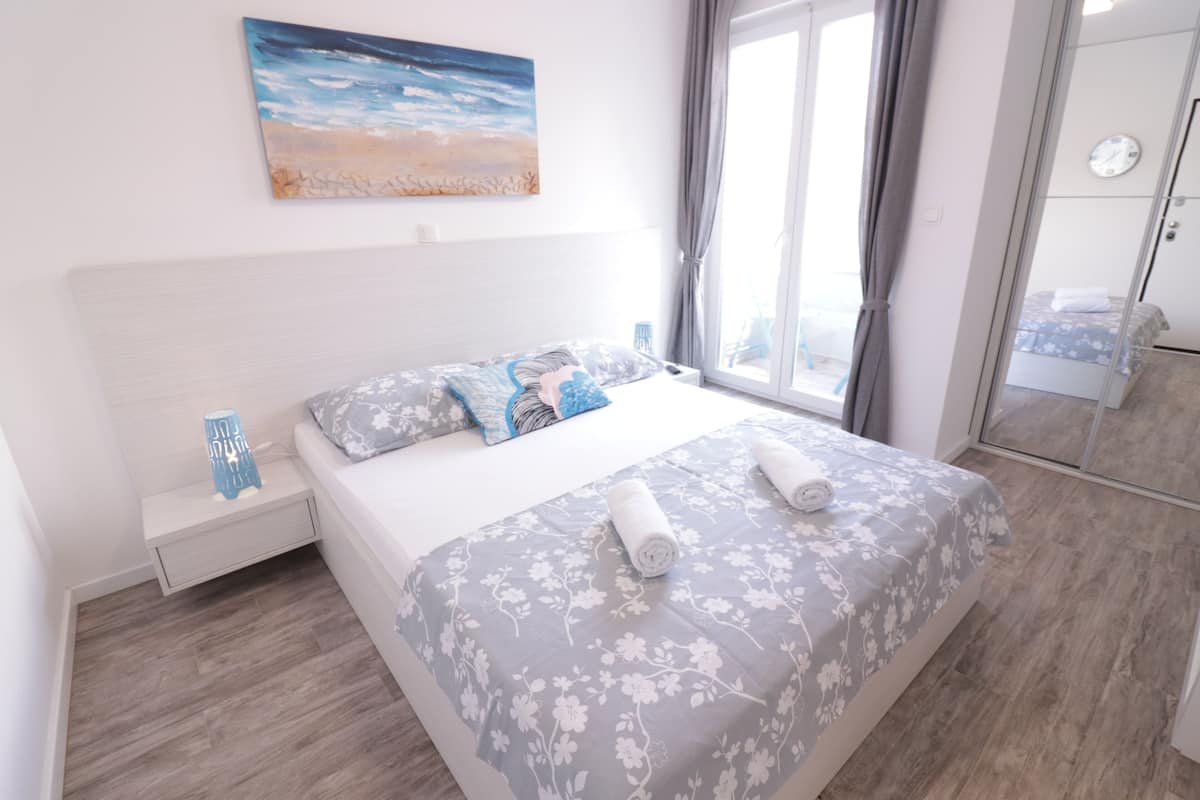 A bedroom with a bed, a nightstand, a painting, and a window with curtains.