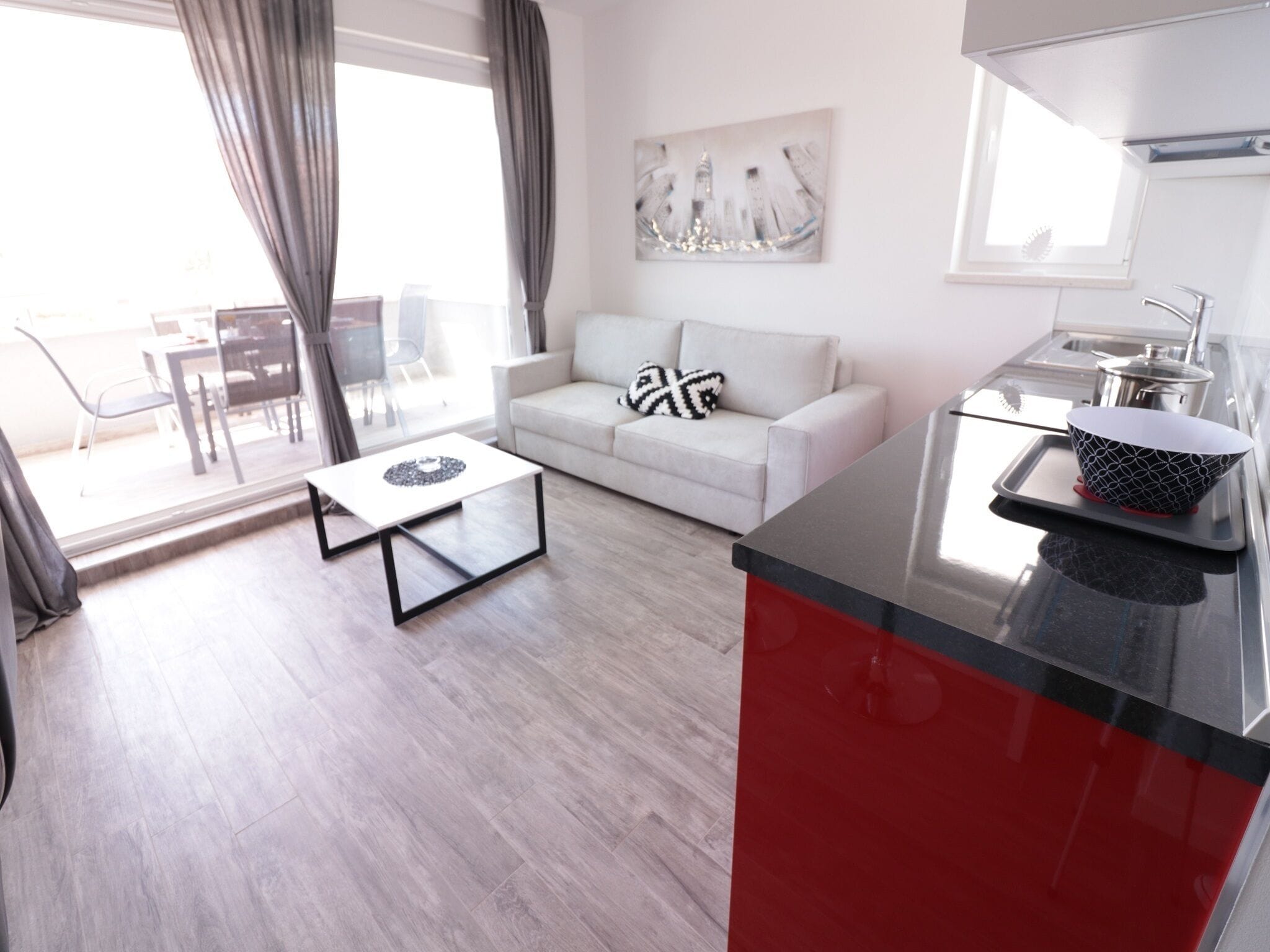 Un salon moderne avec un canapé blanc, une table basse et un coin cuisine doté d’un plan de travail rouge et d’un évier.