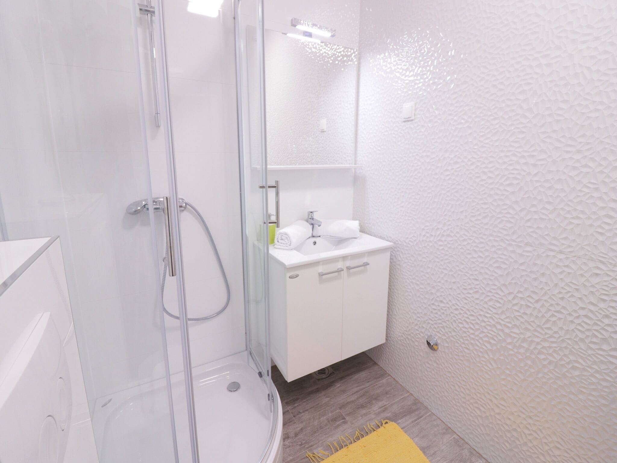 A modern bathroom with a glass-enclosed shower, a white sink, and a yellow rug.