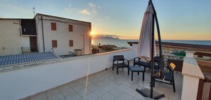 Terraza en la azotea con vista al mar al atardecer, que incluye una mesa y sillas, una pérgola y una barandilla.