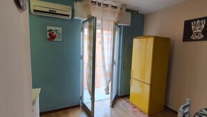 A room with teal walls, a yellow refrigerator, a door leading to an outdoor area, and a small window with a curtain. - View of the gulf of castellammare mountains and beach (Alcamo Marina)