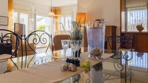 A dining table with a glass top, surrounded by metal chairs, with a vase of plants and a glass pitcher on it. - Vacation home Arenal by Interhome (L'Ampolla)