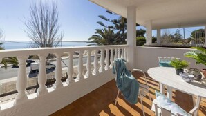 A balcony with a white balustrade, a table with chairs, and a view of the sea and palm trees. - Vacation home Arenal by Interhome (L'Ampolla)