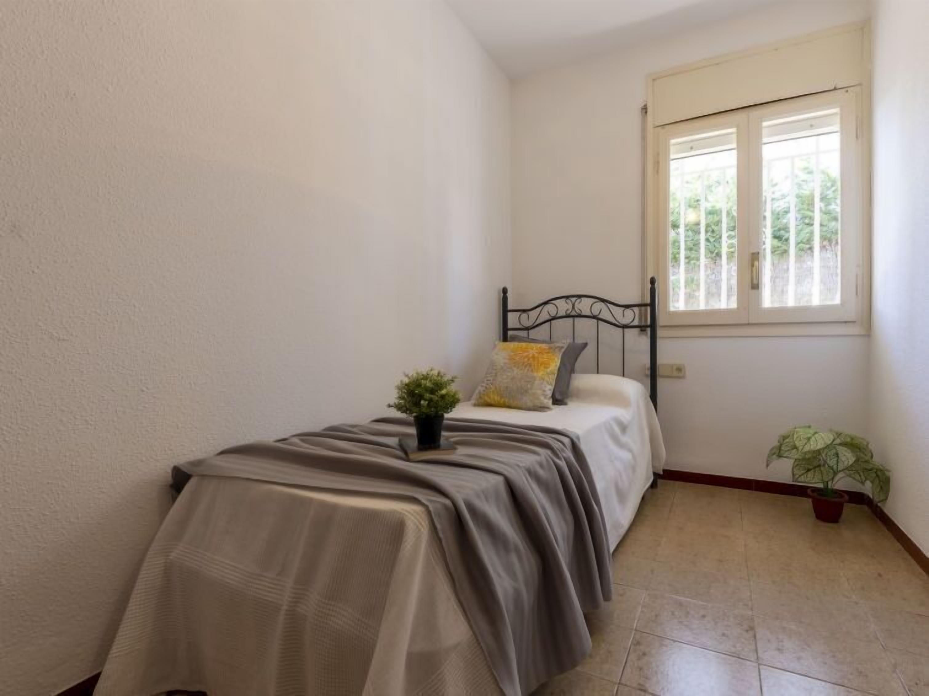 A small, neatly arranged bedroom with a single bed, a window, and a potted plant.