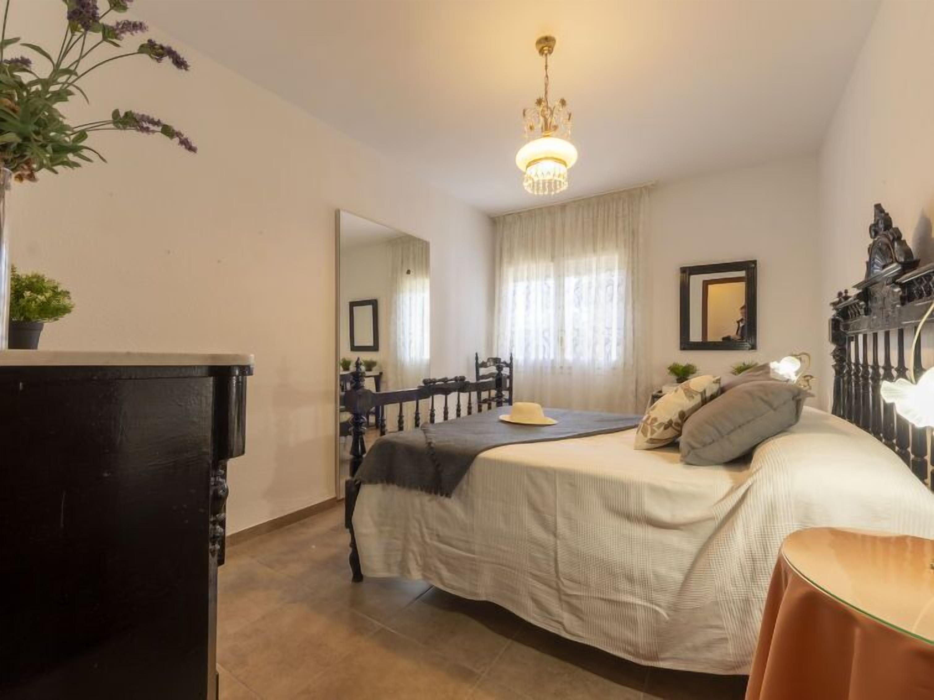 Un dormitorio con cama, cómoda, espejo y una araña.