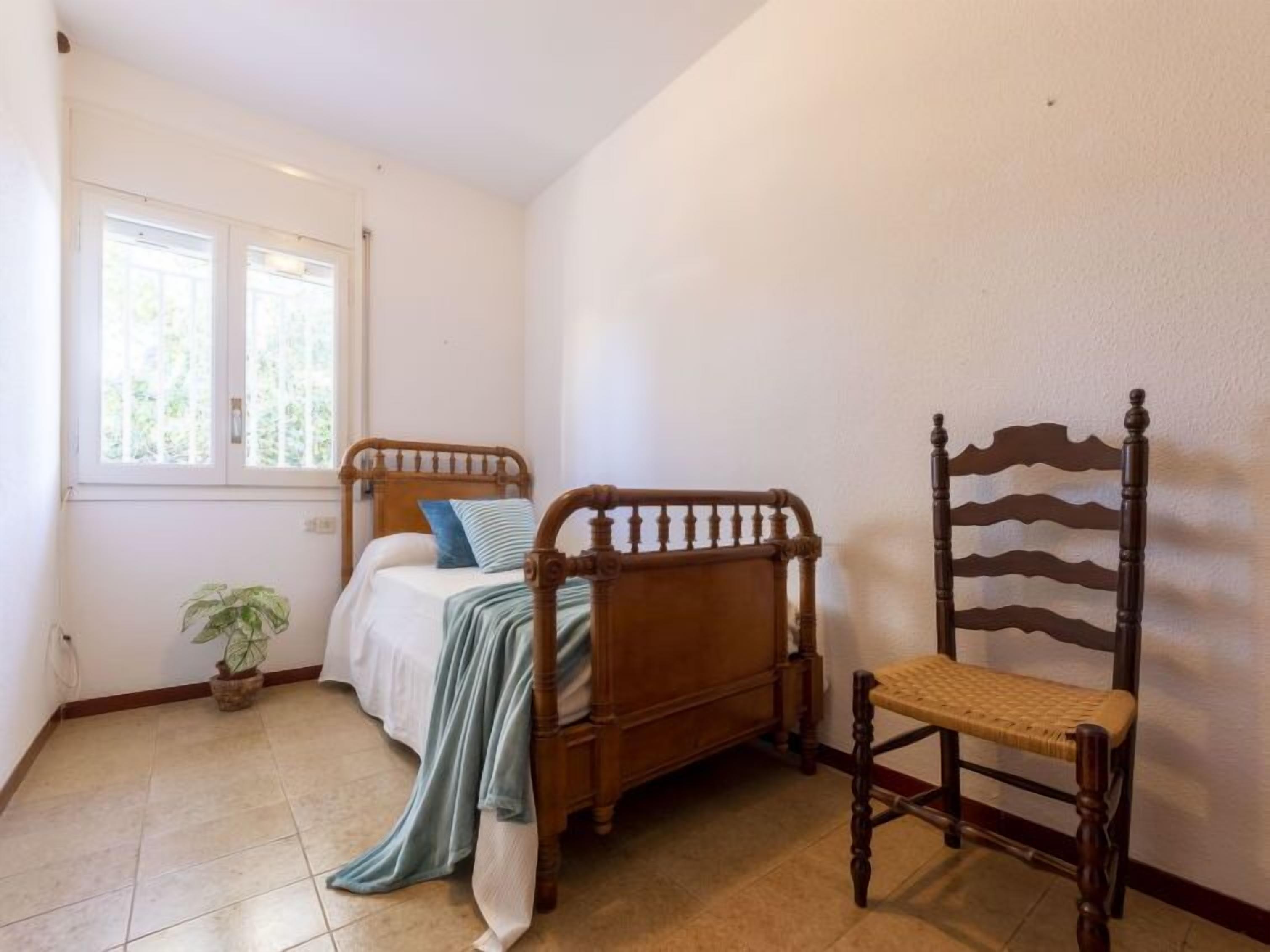 A bedroom with a wooden bed, a chair, a potted plant, and a window.