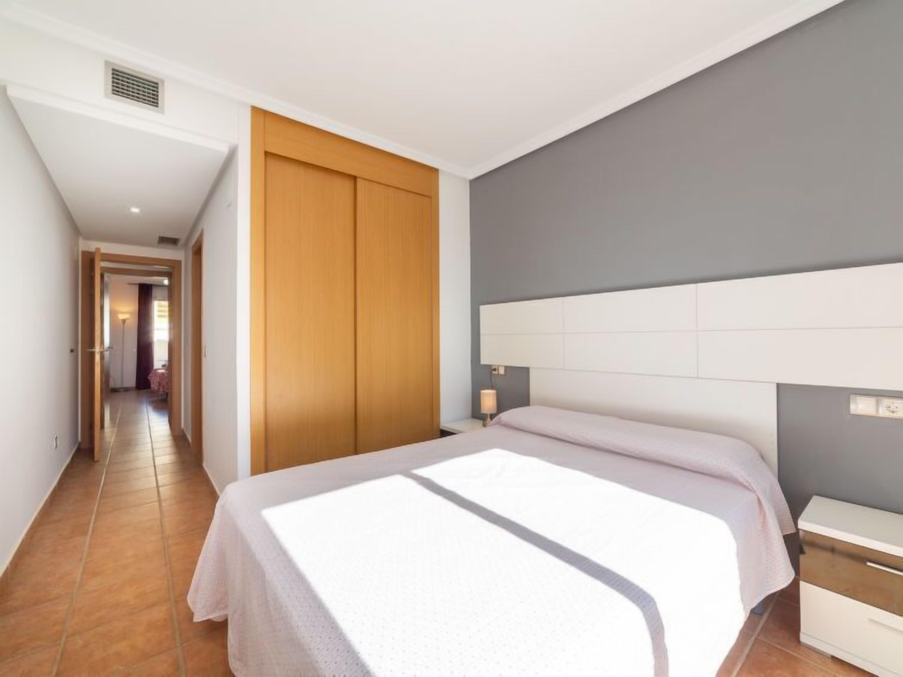 A bedroom with a bed, a nightstand, a wardrobe, and a hallway leading to another room.