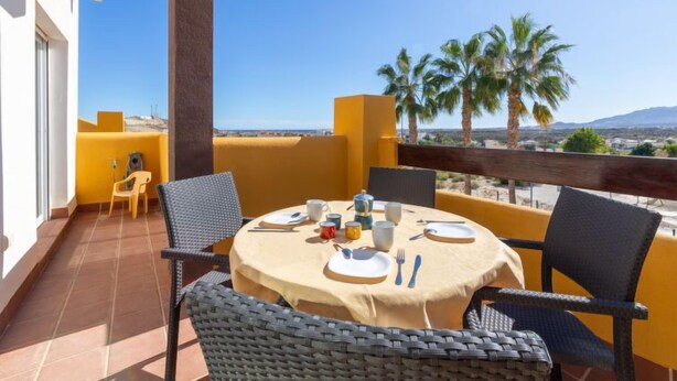 A round table set for two with chairs, a yellow wall, and a view of palm trees and mountains. - Lomas del Mar V by Interhome (Vera)
