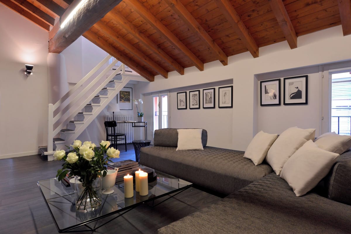 Un salon moderne avec une table basse en verre, un canapé gris et un plafond en bois.