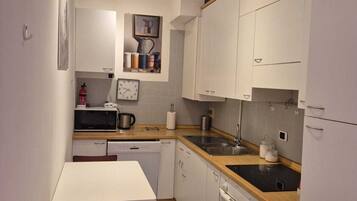 Una cocina compacta con armarios blancos, microondas, fregadero y un rincón comedor con una silla.