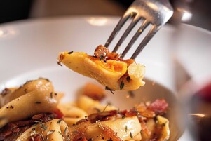 Una forchetta solleva un boccone di cibo con erbe aromatiche e pezzetti di pancetta.