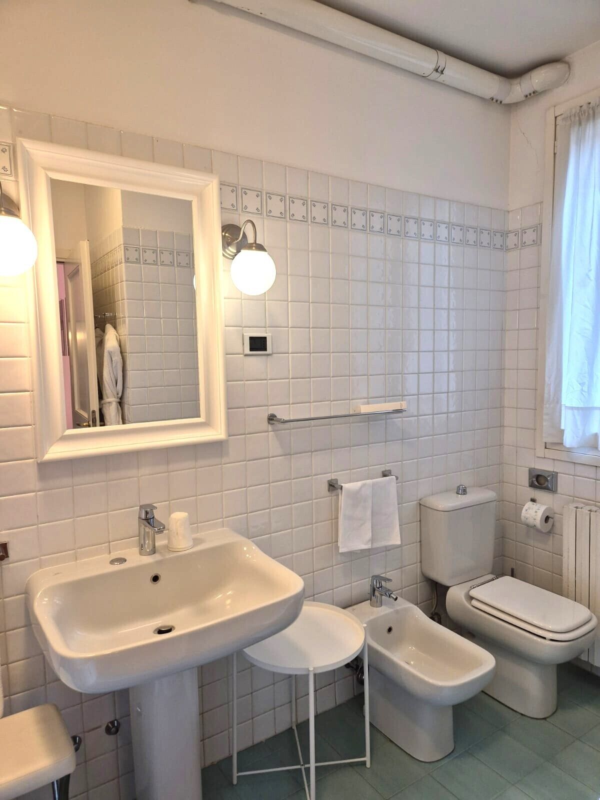 A bathroom with a large mirror, two sinks, a bidet, and a toilet.