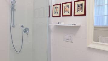 A bathroom with a glass shower enclosure, a toilet, a sink, and three framed pictures on the wall.