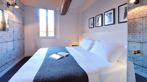 A neatly made bed with a book, a window with blinds, and framed pictures on the wall. -  Phi Hotel Bologna Apartments (Bologna)