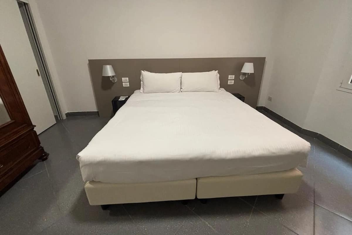 Un grand lit avec une tête de lit, deux tables de chevet et des lampes fixées au mur.