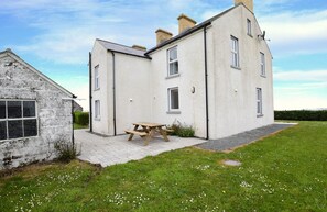 Ein zweistöckiges Haus mit gepflasterter Terrasse und Picknicktisch.