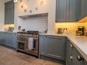 A modern kitchen with grey cabinets, a built-in oven, a stove, and a coffee maker.