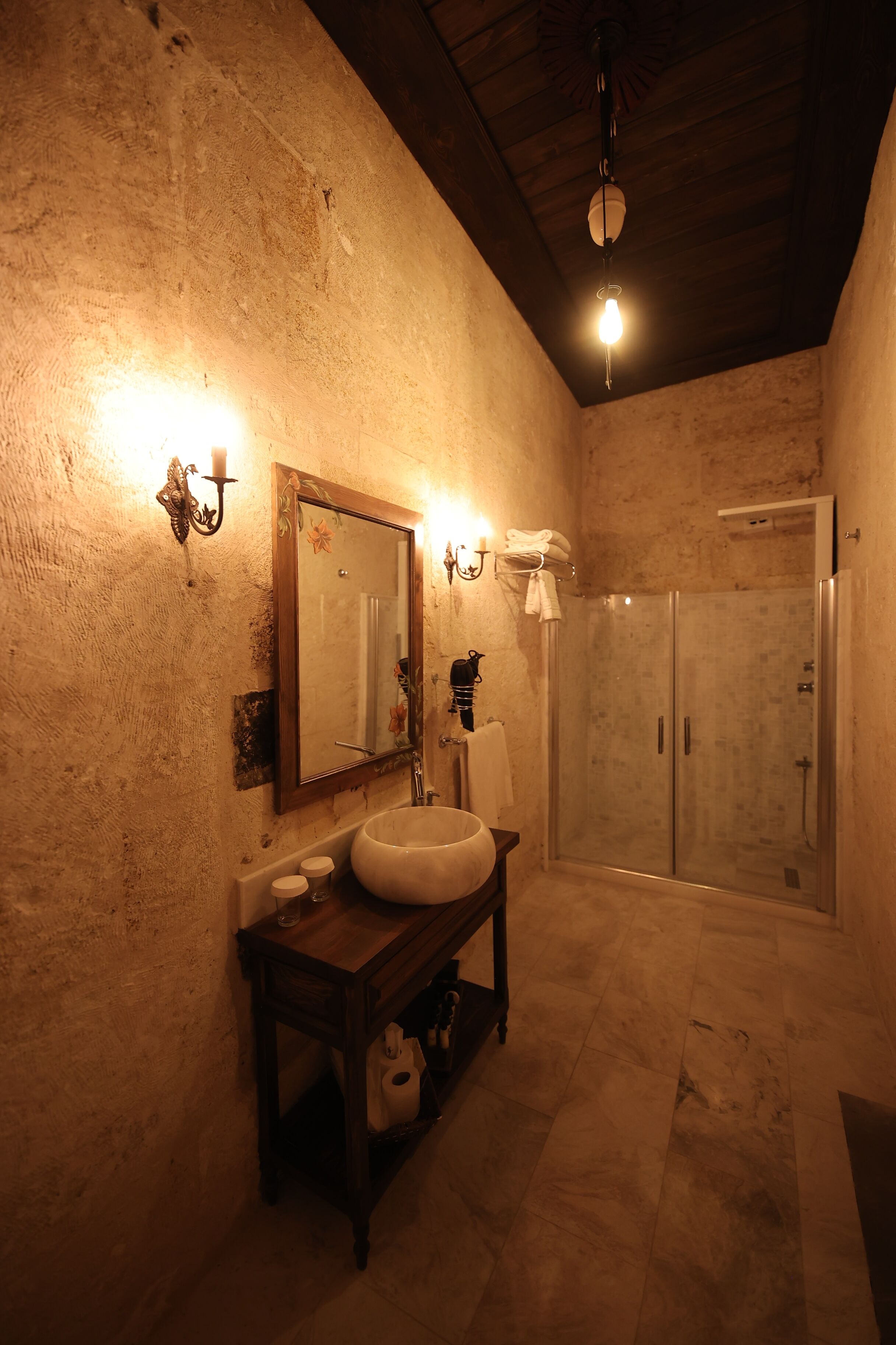 Un baño con diseño rústico, que incluye un espejo grande, un tocador de madera, un lavabo y una ducha con mampara de vidrio.