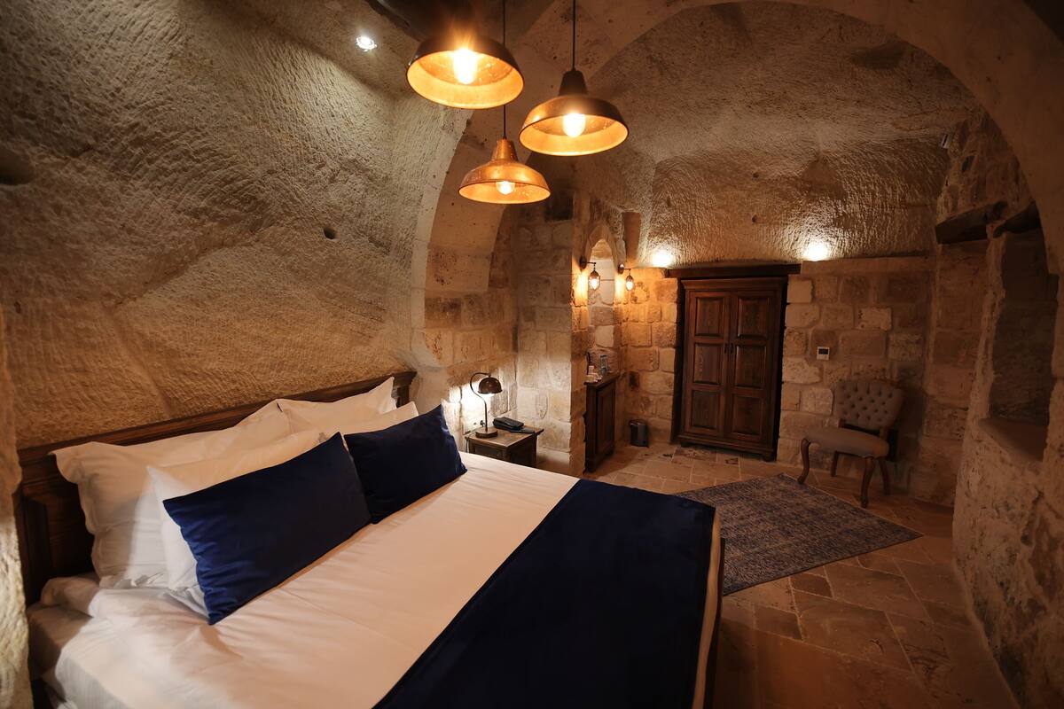 A stone-walled bedroom with a large bed, a wooden wardrobe, and a stone fireplace.