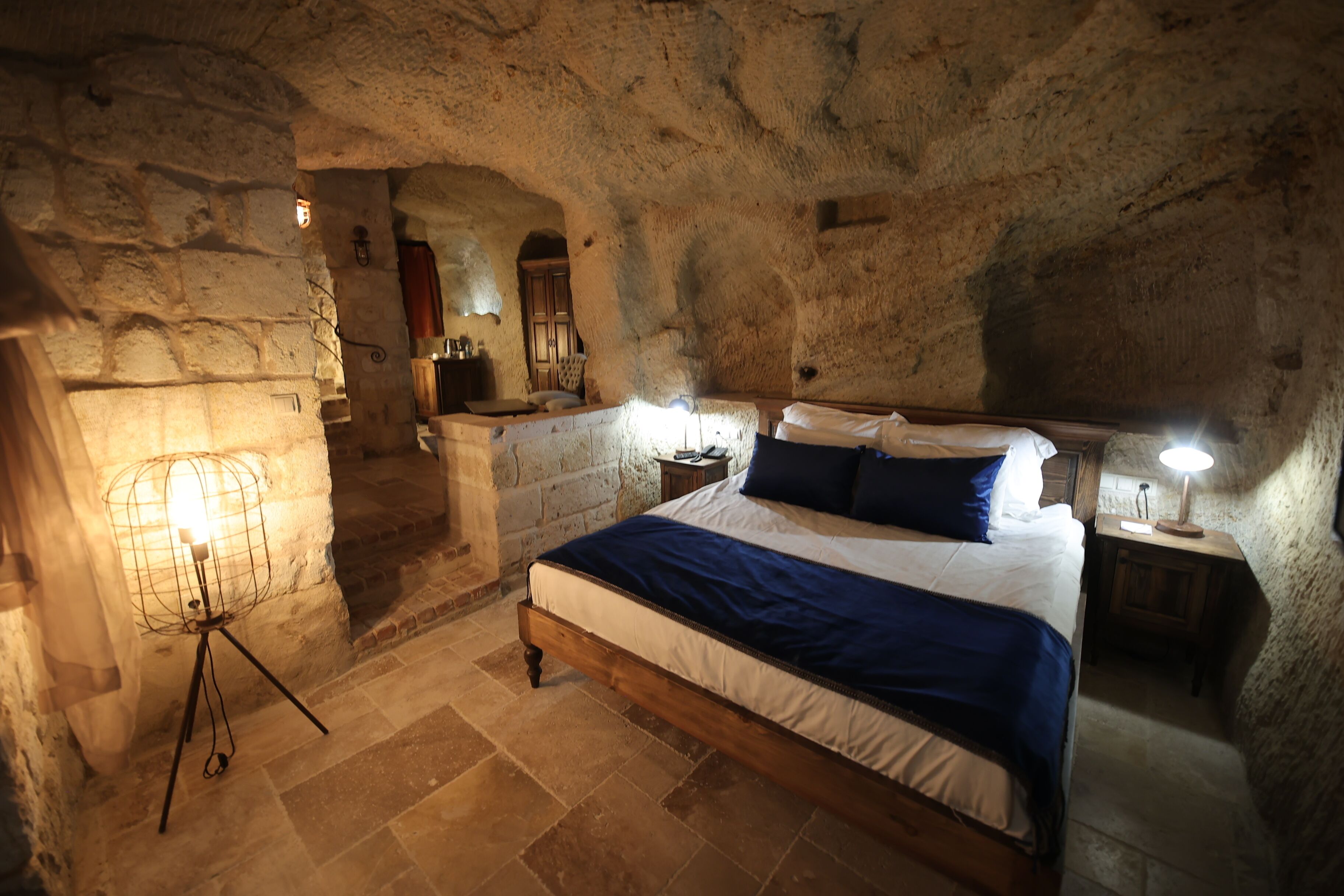 Dormitorio con paredes de piedra, cama, lámparas de noche y lámpara de pie.