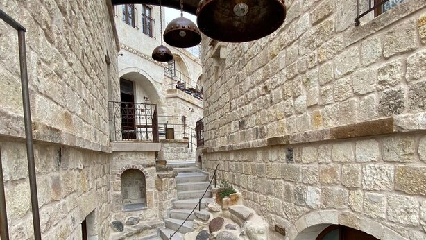 A narrow stone corridor with a staircase leading to an upper level, stone walls, and metal railings.