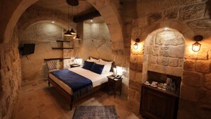A stone-walled bedroom with a bed, bedside tables, and a small cabinet.