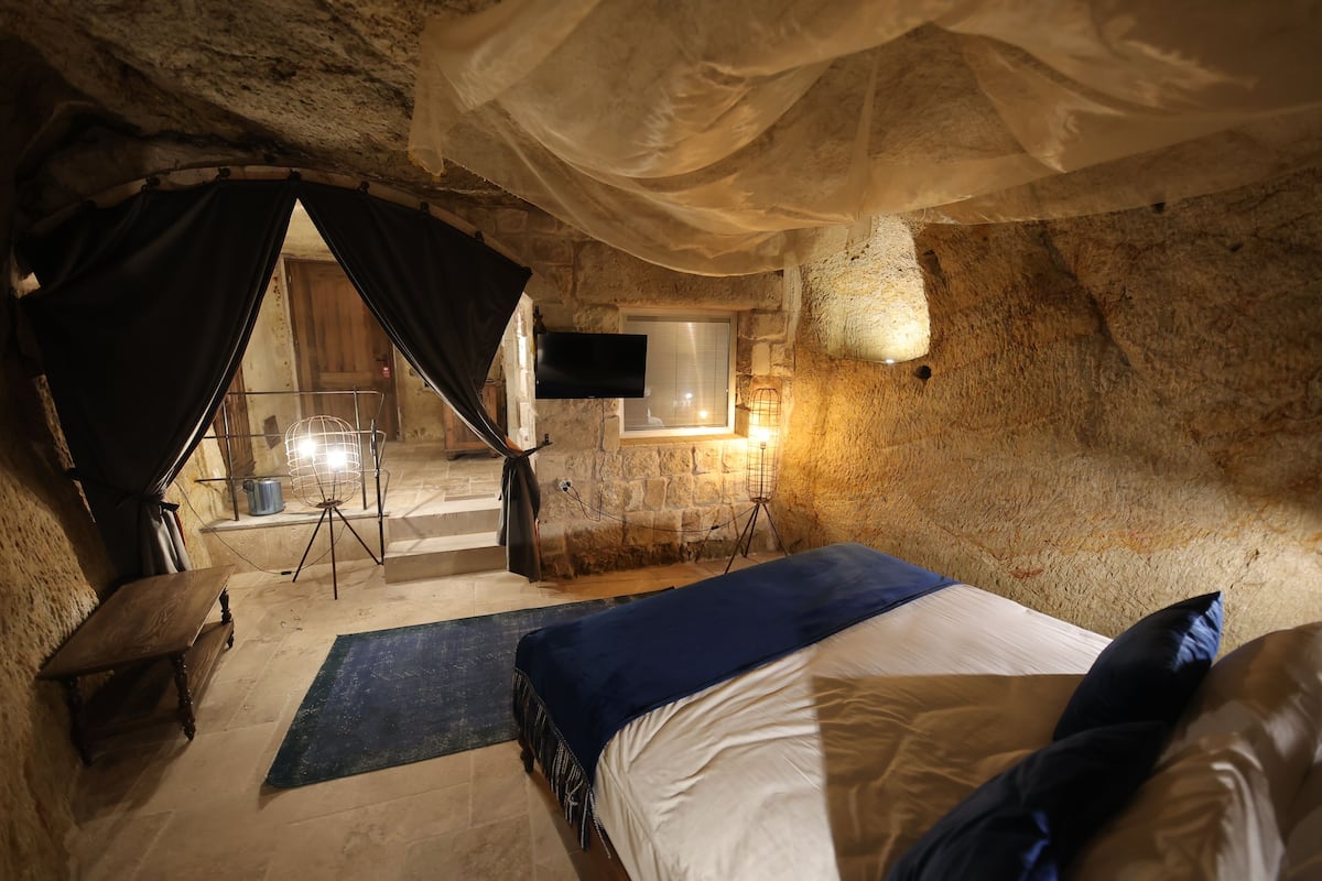 A cozy, rustic room with a bed, a small table, a chair, and a television.