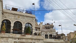 A stone building with arched doorways and a balcony with outdoor seating.