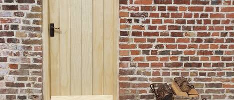A wooden door with a metal handle, a small mailbox, and a stack of firewood on a gravel surface.