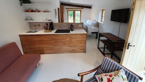 Un espacio habitable compacto con kitchenette, comedor, televisor y ventana.