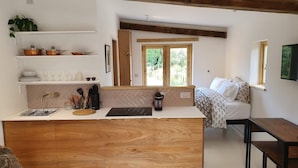 Una cocina compacta con una isla de madera, estantes blancos y una ventana con vistas a zonas verdes.