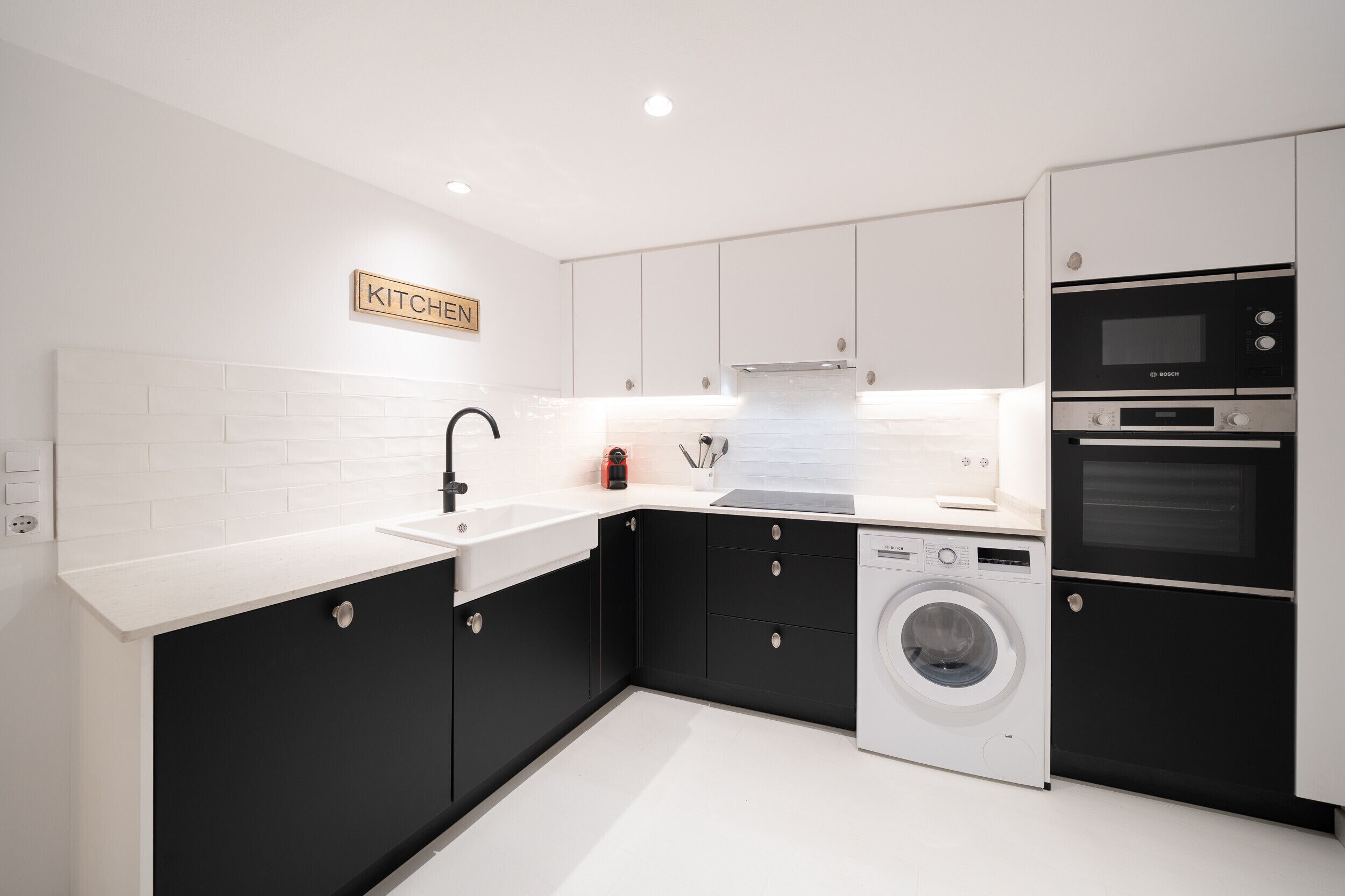 A modern kitchen with white and black cabinetry, a Bosch oven, a washing machine, and a sink.