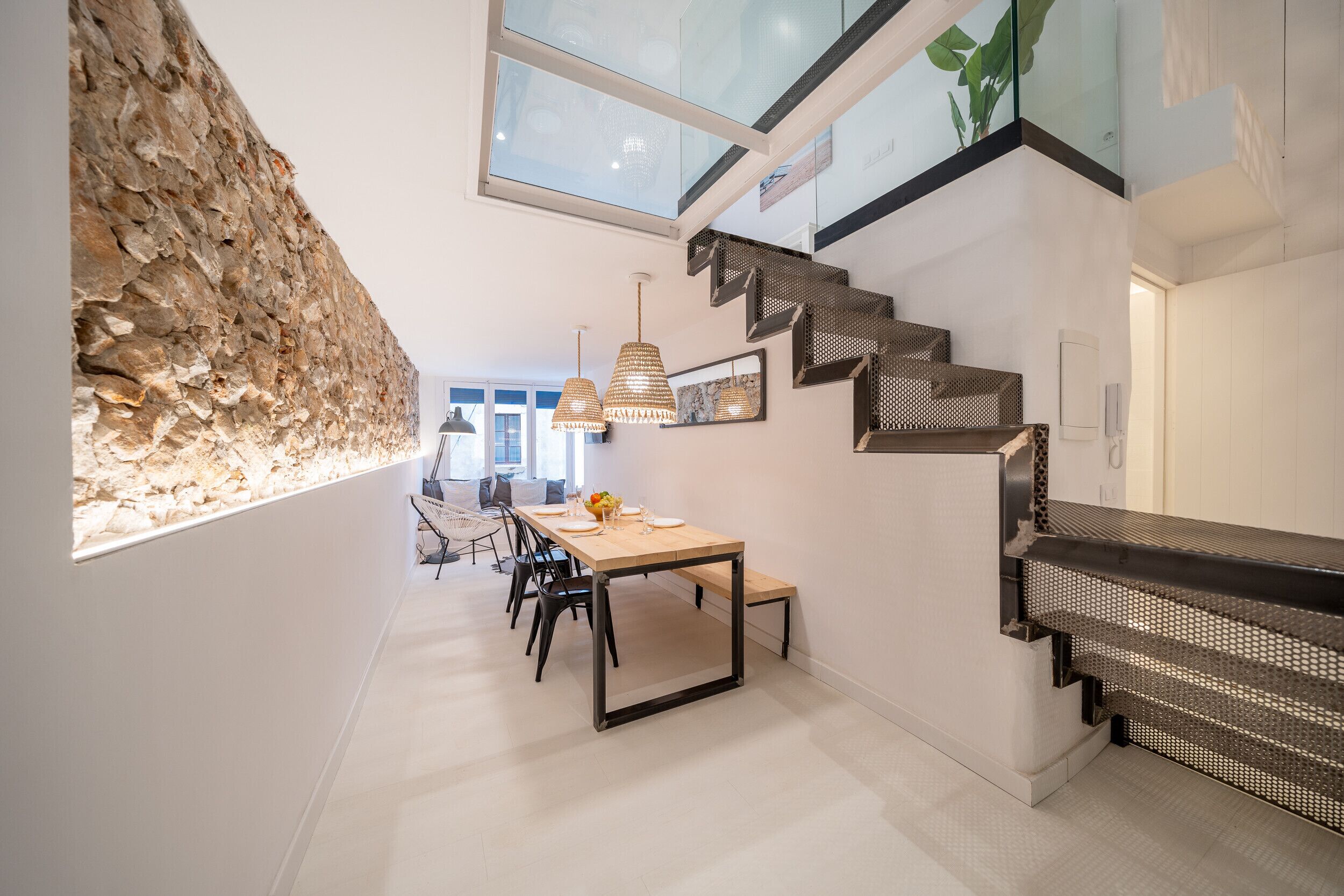 Een modern interieur met een accentmuur van steen, een eethoek met een lange tafel en stoelen, en een trap met een bijzonder ontwerp.