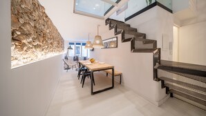 A modern interior with a stone accent wall, a dining area with a long table and chairs, and a staircase with a unique design. - Freya: Apartment in the center of the village (L'Escala)