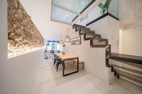 A modern interior with a stone accent wall, a dining area with a long table and chairs, and a staircase with a unique design.