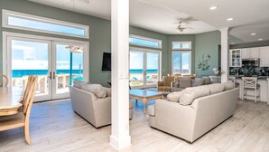 Amplia sala de estar con un ventanal con vista al océano, una cocina con armarios blancos y un comedor con mesa y sillas de madera.