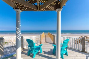 Une terrasse en bois avec deux chaises et une table, donnant sur une plage.