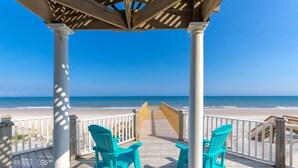 Una terraza de madera con sillas turquesas, una pérgola de madera y vista a la playa.