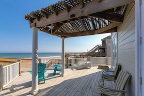 Une terrasse en bois agrémentée d’une pergola, d’un espace salon extérieur et offrant une vue sur l’océan.