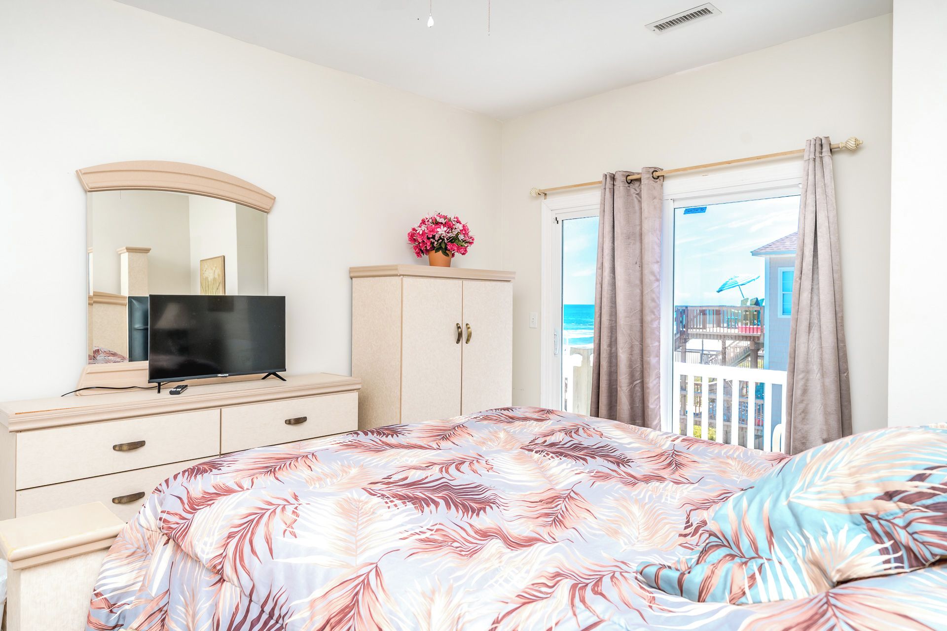A bedroom with a bed, a TV on a dresser, a cabinet, and a view of the sea through a window.
