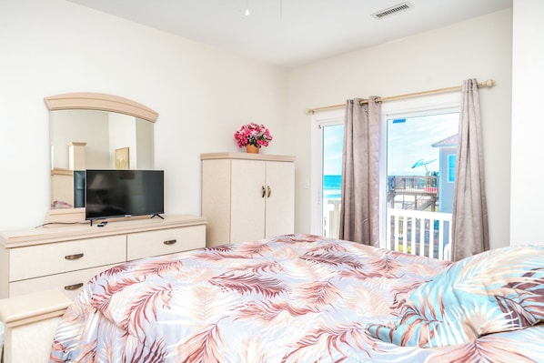 Une chambre à coucher avec un lit, un téléviseur posé sur une commode, un placard et une vue sur la mer par la fenêtre.