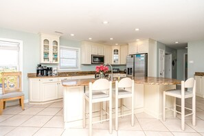 A modern kitchen with white cabinetry, a central island with bar stools, and a stainless steel refrigerator. - @ THE PEACH offers an escape to an oceanfront/oceanside (Sneads Ferry)