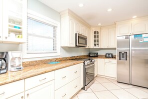 A modern kitchen with white cabinetry, a stainless steel refrigerator, a microwave, a toaster, and a coffee maker. - @ THE PEACH offers an escape to an oceanfront/oceanside (North Topsail Beach)