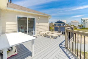 Une terrasse avec une table et des chaises, une porte-fenêtre coulissante donnant sur une pièce, et une vue sur les maisons voisines.