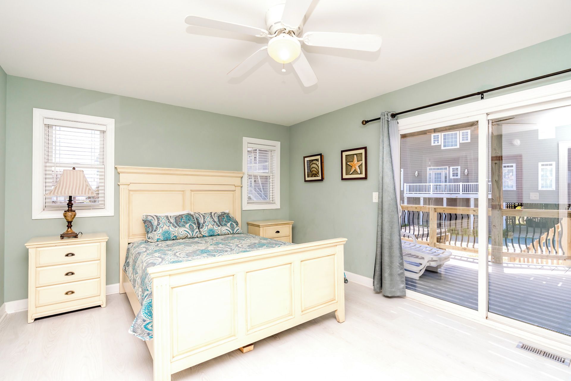A bedroom with a bed, bedside tables, a ceiling fan, and a sliding glass door to a balcony.